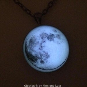 Puede incluir: Un collar con cadena de plata y un colgante de luna de vidrio que brilla en la oscuridad. El colgante de luna tiene una imagen detallada de la superficie de la luna.