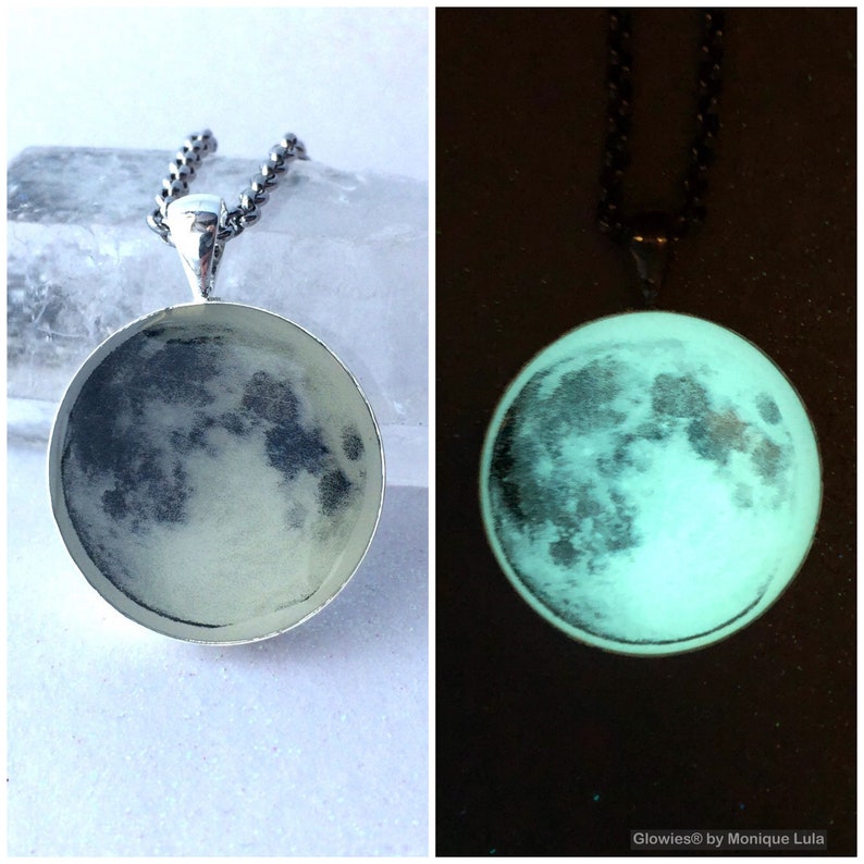 Puede incluir: Un collar de cadena de plata con un colgante redondo que presenta una imagen detallada de la luna. El colgante brilla en la oscuridad, revelando un tono verde.