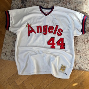 Puede incluir: Camiseta de béisbol blanca con "Angels" en letras rojas y el número "44". La camiseta tiene ribetes rojos y azul marino en las mangas y el cuello. Un pequeño parche es visible en la parte inferior izquierda.