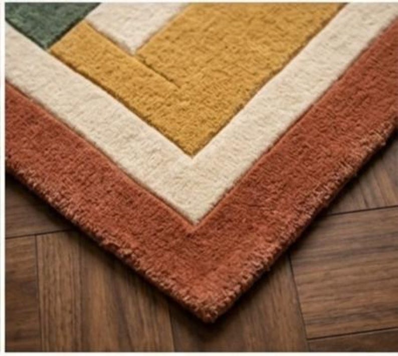 May include: Close-up of a geometric patterned rug with a textured surface. The rug features a color block design with shades of rust, cream, gold, and green. The rug is placed on a wooden floor.
