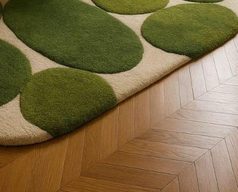 May include: A close-up of a rug with a beige background and green, organic-shaped patterns. The rug is placed on a wooden floor with a herringbone pattern. The rug's design resembles stepping stones.