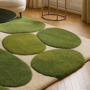 May include: A rectangular rug featuring a cream-coloured background and large, irregularly shaped green circles. The circles vary in shades of green, creating a textured, organic pattern. The rug is placed on a wooden floor.