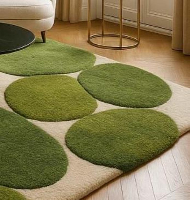 May include: A rectangular rug featuring a cream-coloured background and large, irregularly shaped green circles. The circles vary in shades of green, creating a textured, organic pattern. The rug is placed on a wooden floor.