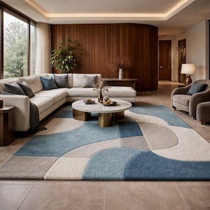 Könnte beinhalten: Ein großer Teppich mit einem geometrischen Muster aus überlappenden Kreisen und Kurven in Blau-, Creme- und Grautönen. Der Teppich liegt in einem Wohnzimmer mit einem beigen Ecksofa, einem runden Marmor-Couchtisch und einem grauen Sessel.
