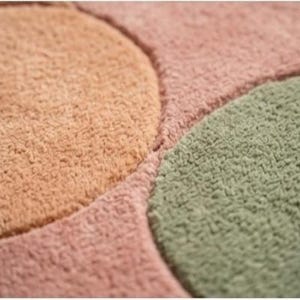May include: Close-up of a soft, textured rug with a geometric design. The rug features sections of peach, pink, and green, creating a colorful and inviting pattern. The plush material suggests comfort and warmth.