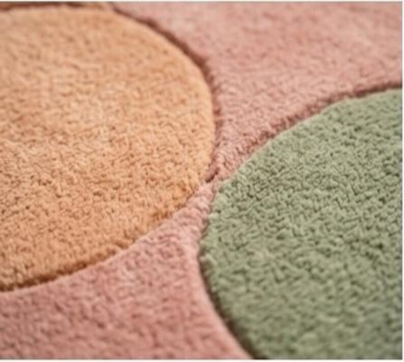 May include: Close-up of a soft, textured rug with a geometric design. The rug features sections of peach, pink, and green, creating a colorful and inviting pattern. The plush material suggests comfort and warmth.