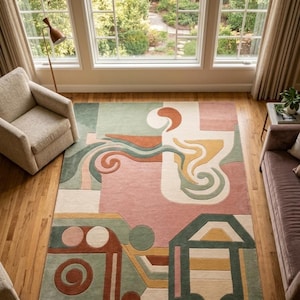 May include: A large, rectangular area rug with an abstract design in shades of pink, green, orange, and cream. The rug features geometric shapes and swirling patterns, creating a modern and artistic look. The rug is placed on a hardwood floor.