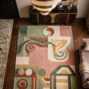 May include: A large rectangular rug with an abstract design in shades of pink, green, orange, and cream. The rug features geometric shapes and flowing lines, creating a modern and artistic aesthetic. The rug is placed on a dark wood floor.