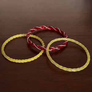 May include: Three twisted glass bangles, one red with white stripes, two yellow with white stripes.