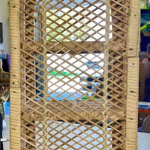 May include: A tall, arched, light tan wicker shelf unit featuring a woven lattice pattern on the sides and back. The structure includes three horizontal shelves and is constructed from natural reed material with a rounded top frame design.