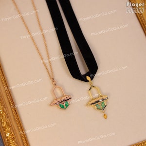 May include: Two gold necklaces with green and gold pendants. The pendants are shaped like a small box with a scroll inside. One necklace has a black velvet cord and the other has a gold chain.