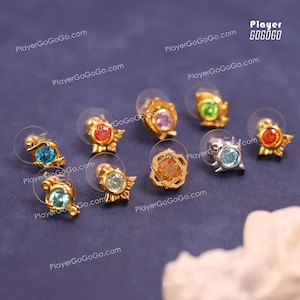 May include: Nine pairs of gold and silver stud earrings with colourful gemstones. The earrings feature various designs, including a swirl, a star, a square, and a flower. The gemstones are blue, green, red, orange, and pink.