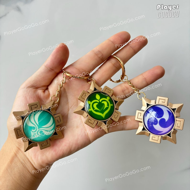 Pu&ograve; includere: Tre portachiavi dorati con simboli di colori diversi. I simboli sono un cuore verde, un fiore turchese e un vortice viola. I portachiavi sono su una mano.