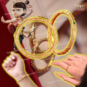 Op de afbeelding: Twee gouden armbanden met ingewikkelde ontwerpen, met een slangmotief en groene accenten. De armbanden worden getoond op een rood oppervlak.