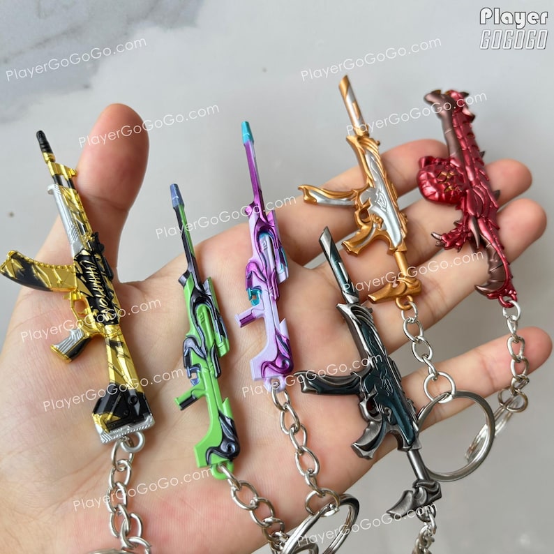 K&ouml;nnte beinhalten: Ein Set aus sechs Schl&uuml;sselanh&auml;ngern mit verschiedenen Waffendesigns. Die Schl&uuml;sselanh&auml;nger sind aus Metall und in verschiedenen Farben gehalten, darunter Gold, Silber, Schwarz, Gr&uuml;n, Lila und Rot. Die Schl&uuml;sselanh&auml;nger sind alle an silbernen Ketten befestigt.