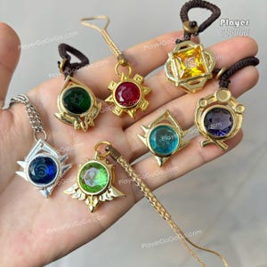 May include: Set of seven gold-tone charms with different colored gemstones. Each charm features a different symbol and a small gemstone in the center. The charms are on a variety of cords and chains.
