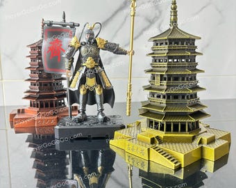 May include: A black and gold figurine of a warrior holding a spear stands on a black base. The warrior is wearing a black and gold armor and a red and gold cape. The figurine is in front of a gold pagoda with a black roof. The pagoda is on a gold base with the text "应县木塔" in black.