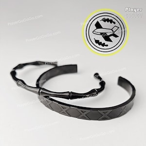 May include: Two black metal bracelets. One has a bamboo-style design, the other a geometric pattern. A circular emblem with a plane graphic and the text "Player GoGoGo" is also visible.