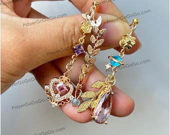 May include: Gold-toned dangle earrings with intricate floral and celestial designs. One earring features a heart-shaped pendant with a pink gem, while the other has a planet charm and a teardrop-shaped gem. Both earrings have leaf and rose details.