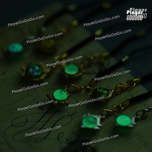 May include: A collection of seven glow-in-the-dark charms with a green glow. The charms are attached to black cords and feature different designs. The charms are on a dark surface with the text "PlayerGoGoGo.com" repeated multiple times.