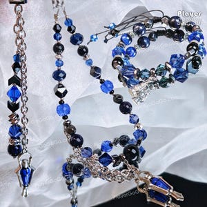 May include: A jewelry set featuring a necklace, bracelet, and dangling charm, all crafted with deep blue and black beads, faceted crystals, and silver-toned metal chains. The pieces include small lantern-shaped pendants with blue inserts.