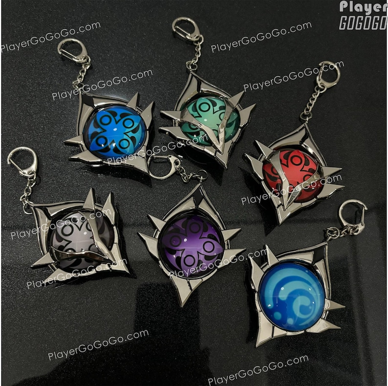 K&ouml;nnte beinhalten: F&uuml;nf silberne Schl&uuml;sselanh&auml;nger mit verschiedenen farbigen Designs. Jeder Schl&uuml;sselanh&auml;nger hat einen silbernen Metallrahmen mit einem kreisf&ouml;rmigen Design in der Mitte. Die Designs sind blau, gr&uuml;n, rot, lila und blau. Die Schl&uuml;sselanh&auml;nger sind in einem Kreis auf einer schwarzen Oberfl&auml;che angeordnet.