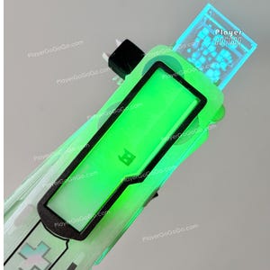 Può includere: Un dispositivo di gioco portatile con uno schermo verde neon e un bordo nero. Il dispositivo ha un corpo verde traslucido con un piccolo schermo nella parte superiore e il testo "Player GoGoGo" sullo schermo superiore.