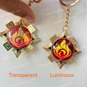 Pu&ograve; includere: Due portachiavi dorati con un designo a fiamma rosso e giallo. Il portachiavi a sinistra ha uno sfondo trasparente, mentre il portachiavi a destra ha uno sfondo luminoso. Il testo "Player GOGOGO" &egrave; visibile nell'angolo in alto a destra dell'immagine.