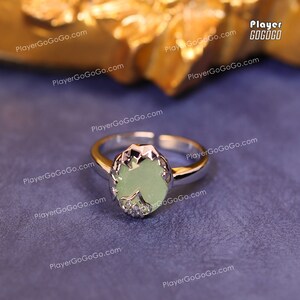 May include: A silver ring with a light green oval-shaped stone set in a silver setting. The stone is surrounded by a silver design.