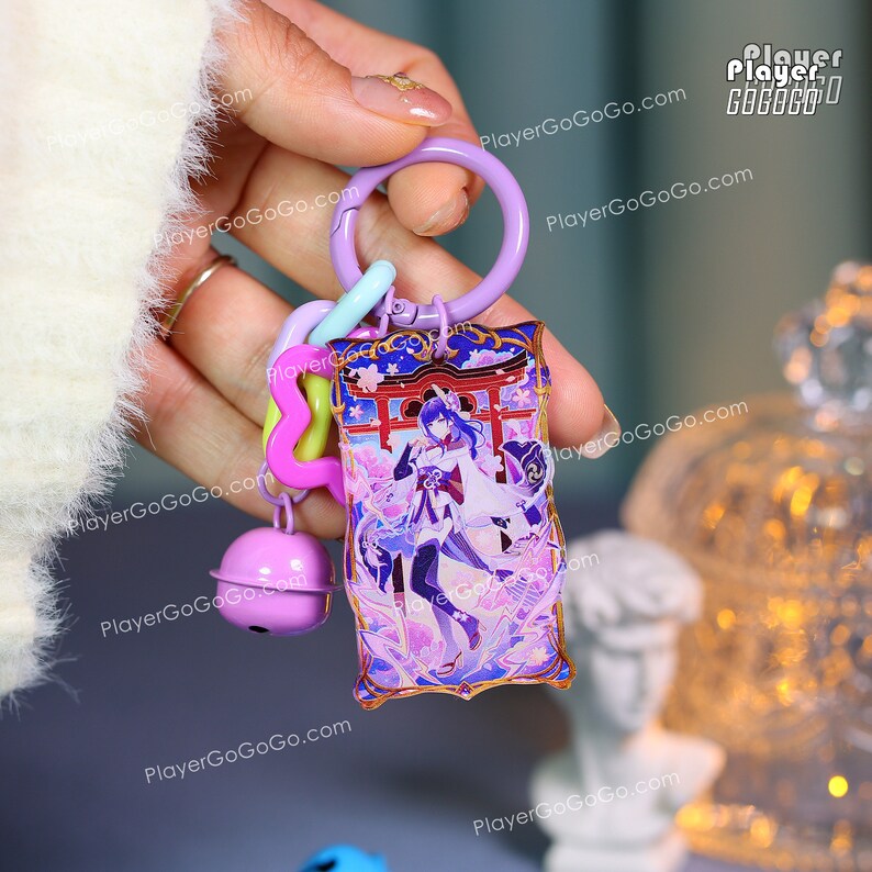 Puede incluir: Un llavero morado con un dije rectangular con una ilustraci&oacute;n de personaje. El dije tiene un borde dorado y un dise&ntilde;o con colores morado, azul y blanco. El llavero incluye un anillo morado, un cierre azul claro y una campana rosa.