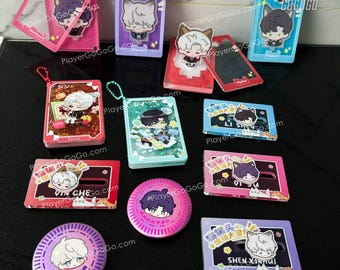 May include: A collection of colorful acrylic charms featuring anime characters. The charms are in various shapes and sizes, including square, round, and rectangular. Some charms have glitter accents. The charms are displayed on a table with a white background.