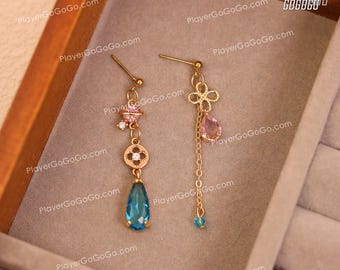 Könnte beinhalten: Ein Paar goldene Ohrringe mit blauen und rosa Edelsteinen. Ein Ohrring hat einen tropfenförmigen blauen Edelstein, einen Glückskleeblatt-Anhänger und einen kleinen rosa und weißen Planeten-Anhänger. Der andere Ohrring hat einen tropfenförmigen rosa Edelstein und einen rosa Blumen-Anhänger.