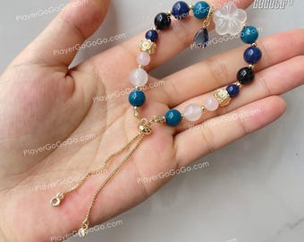 May include: A blue, pink, and black beaded bracelet with a gold charm and a white flower charm. The bracelet has a gold chain with a sliding clasp.