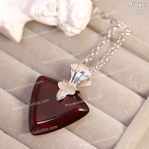 May include: A silver chain necklace with a triangular red gemstone pendant. The pendant has a silver filigree design.