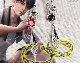 May include: Silver-toned earrings with a red gemstone and a black gemstone. The earrings have a teardrop design and are paired with a woven silver bracelet. The background is a light beige fabric.