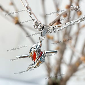 May include: A silver necklace with a pendant featuring a red gemstone surrounded by silver flames. The pendant is attached to a silver chain with a lobster clasp.