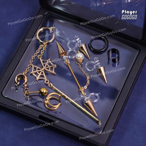 Op de afbeelding: Een set gouden en zwarte oorbellen in een zwarte doos. De oorbellen omvatten een spinnenwebontwerp, een hoepel, een oorbel en een clip-oorbel. De doos heeft de tekst "Player GOGOGO" erop.