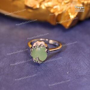 May include: A silver ring with a green gemstone set in a decorative silver setting. The ring is on a purple background.
