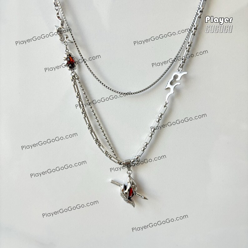 May include: A silver layered necklace with a red stone pendant. The pendant features a stylized design with a sword and a wing. The necklace has a chain with a box clasp. The necklace is on a white background. PlayerGoGo.com is printed on the background.