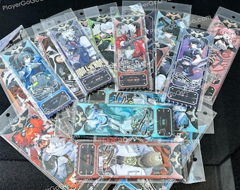 May include: A collection of colourful anime character trading cards in protective plastic sleeves. The cards feature various characters with different hairstyles and clothing. The cards have Japanese text on them.