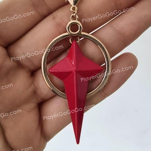 May include: A gold hoop earring with a red star-shaped pendant. The star has a pointed tip and a shiny finish.