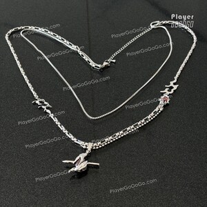 May include: A silver layered necklace with a red stone pendant. The pendant features a stylized design with a wave-like pattern. The necklace is made of three different chain styles.