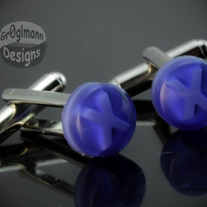 May include: A pair of silver cufflinks with blue glass insets. Each inset features a white letter "X" in a raised design.