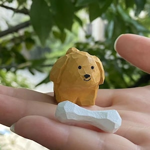 May include: A hand holding a small wooden dog figurine with a white bone. The dog is light brown and has a painted face.