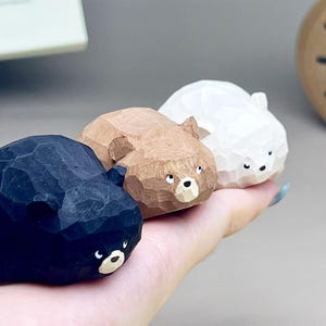 May include: Three small, hand-carved wooden bear figurines in black, brown, and white. Each bear features a faceted, geometric texture across its surface, small rounded ears, and a painted face with a light-colored snout and dark eyes.