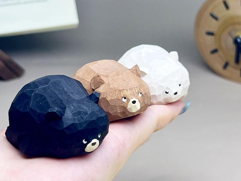 May include: Three small, hand-carved wooden bear figurines in black, brown, and white. Each bear features a faceted, geometric texture across its surface, small rounded ears, and a painted face with a light-colored snout and dark eyes.