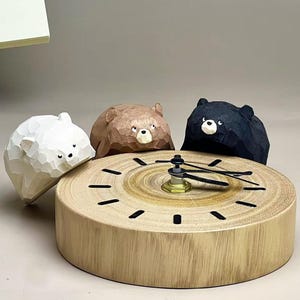 May include: A round wooden clock featuring a natural wood grain face with black hour markers and black hands. Three carved wooden bear figures in white, brown, and black are positioned around the top edge of the clock, each with a faceted texture.