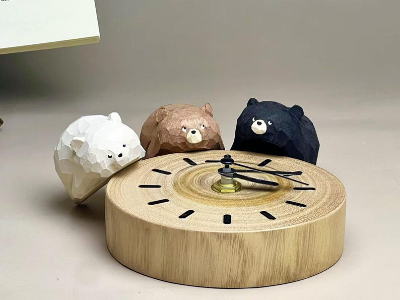 May include: A round wooden clock featuring a natural wood grain face with black hour markers and black hands. Three carved wooden bear figures in white, brown, and black are positioned around the top edge of the clock, each with a faceted texture.