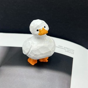 May include: A small, white wooden duck figurine with orange feet and beak. The duck is standing on a white surface.