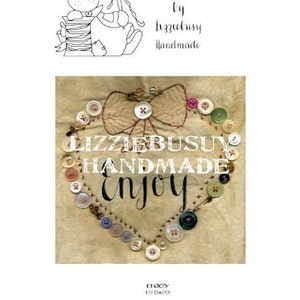 Könnte beinhalten: Ein herzförmiges Design aus Knöpfen und Stickerei auf einem beigefarbenen Stoffhintergrund. Der Text "Lizziebusuy Handmade Enjoy" ist in schwarzem Faden gestickt.